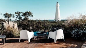 A wooden deck with white chairs and a table, an umbrella, and a view of the sea. - Breathtaking Dome with Spectacular Outdoor Living and Chic Elegant Interior in Texas (Fischer)