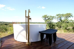 Un jacuzzi en una terraza de madera con vistas a árboles y un paisaje distante.