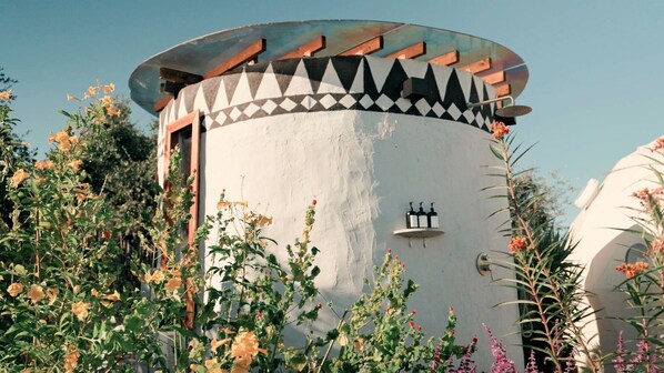 Un edificio cilíndrico con techo decorado, rodeado de diversas plantas y flores.