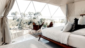 A tented room with a bed, a chair, and a view of the outdoors.