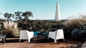 Une terrasse en bois avec des chaises blanches et une table, un parasol et une vue sur la mer.