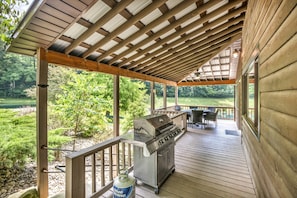 A covered outdoor deck with a grill, seating area, and a view of a natural landscape.