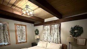 Una camera da letto con copriletto a quadretti, travi in legno a soffitto, un lampadario e una finestra con tende floreali.