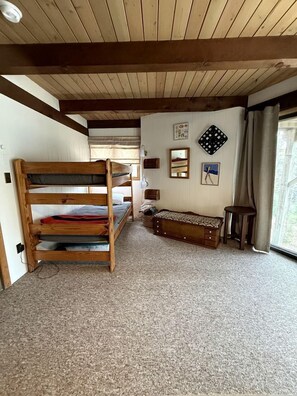 A bunk bed room with a wooden ceiling, a bench, and a window with curtains.