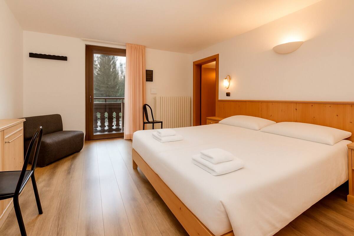 A bedroom with a large bed, a wooden headboard, a desk with a chair, and a view of the outdoors through a glass door.