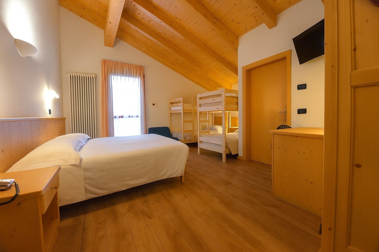 Ein Schlafzimmer mit einem großen Bett, Etagenbetten, einem Schreibtisch, einem Stuhl, einem Fernseher und einem Fenster mit Vorhängen.