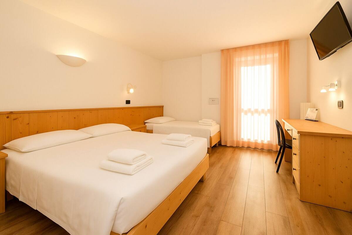 A hotel room with a large bed, a smaller bed, a desk, and a TV.