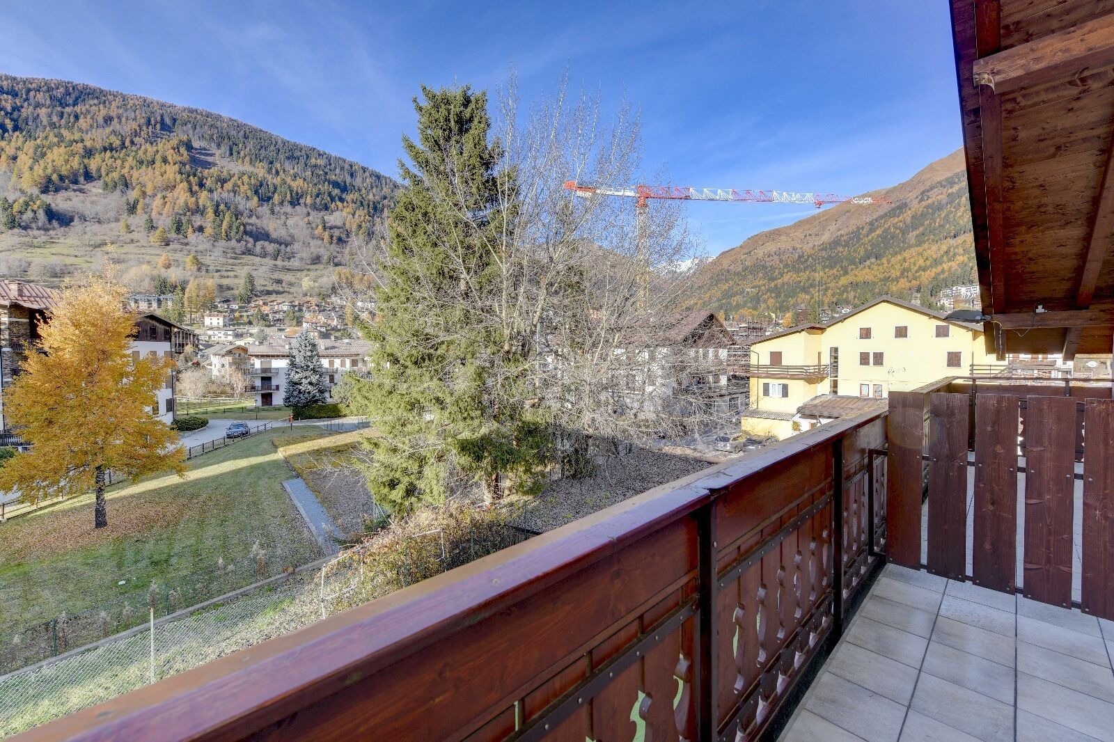 A balcony with a view of a town, a construction crane, and a mountain in the background.