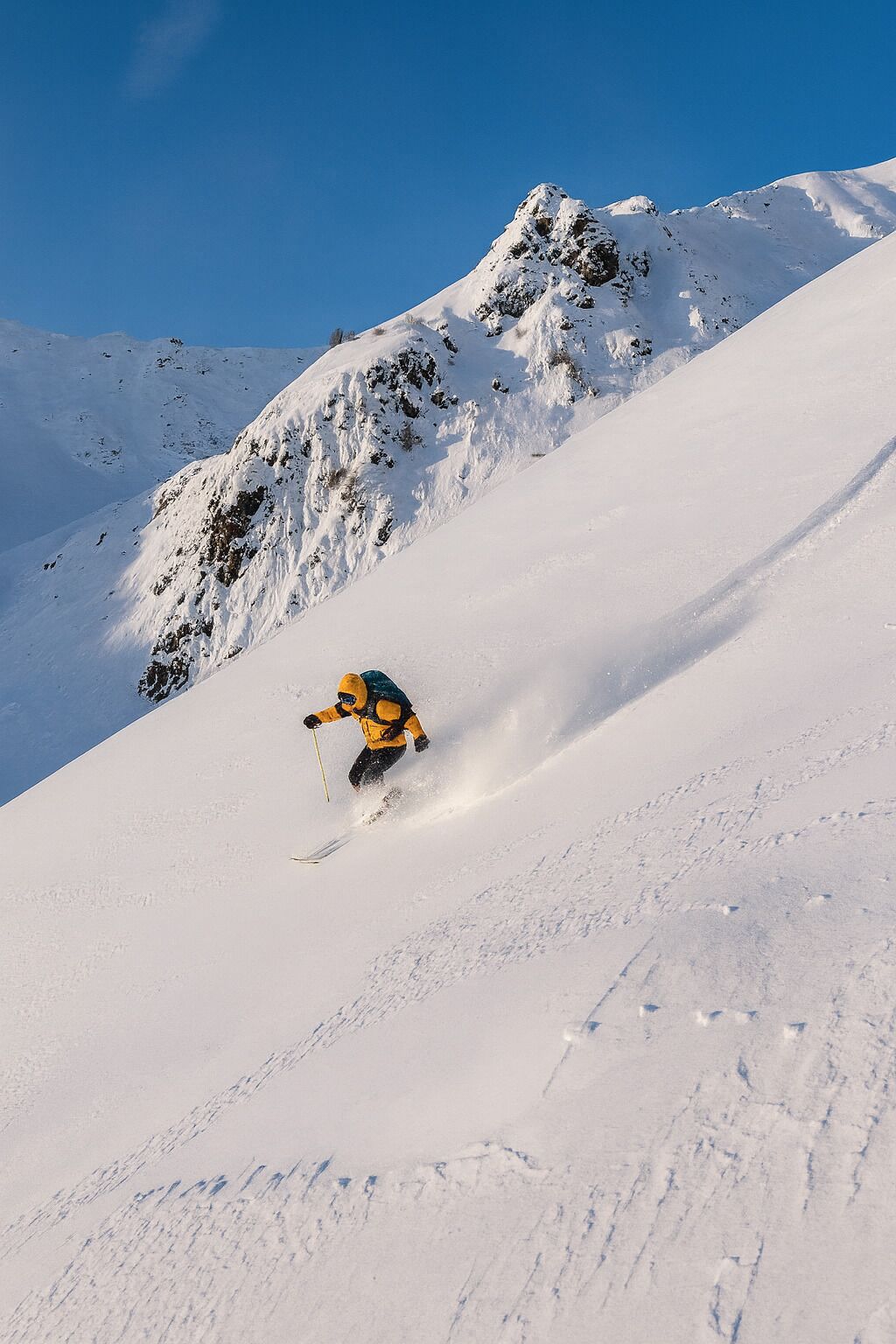 A skier on a snow-covered slope with rocky outcrops in the background.