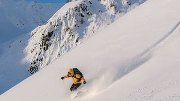 A skier on a snow-covered slope with rocky outcrops in the background.
