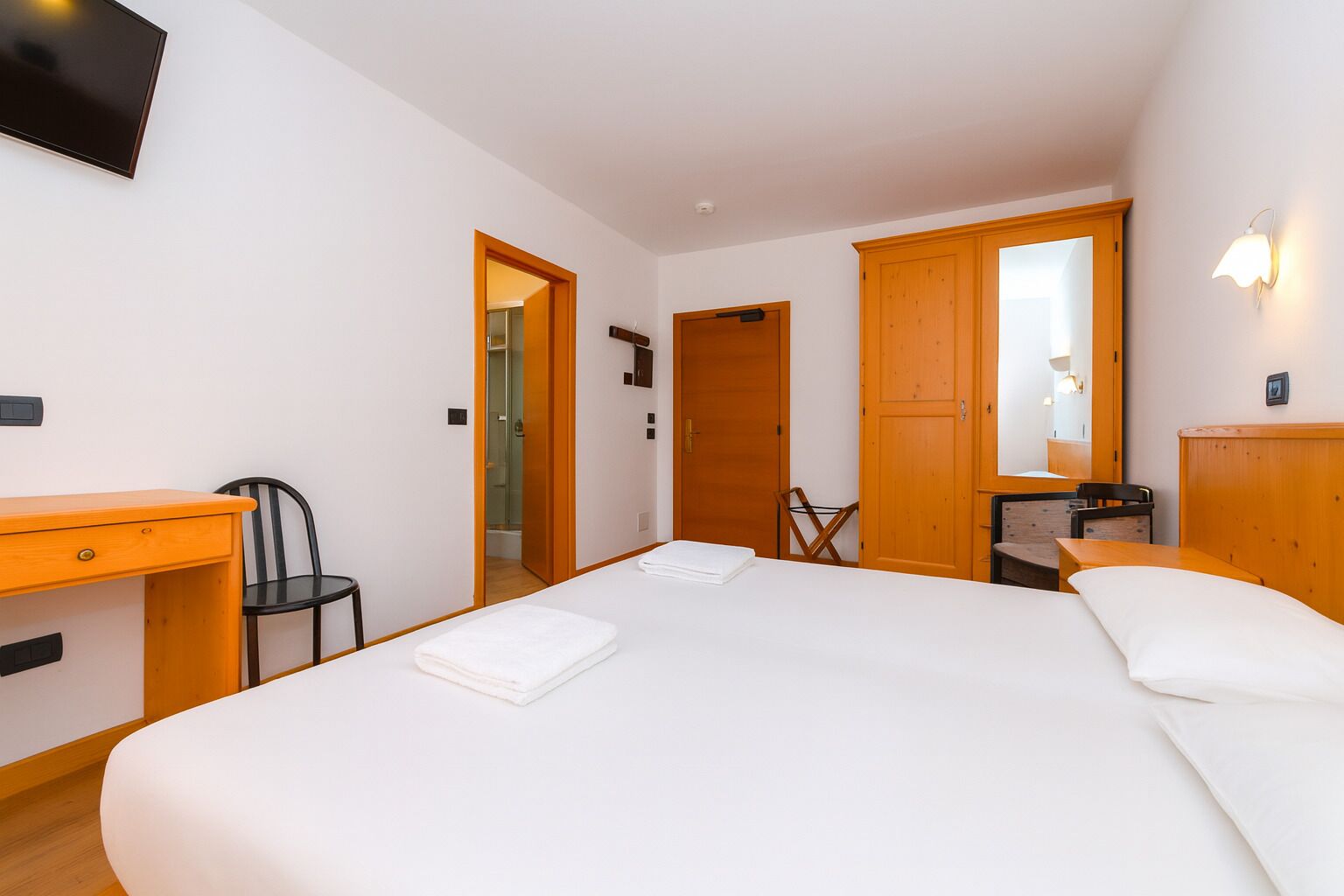 Een hotelkamer met een groot bed, een bureau, een stoel en een televisie aan de muur.