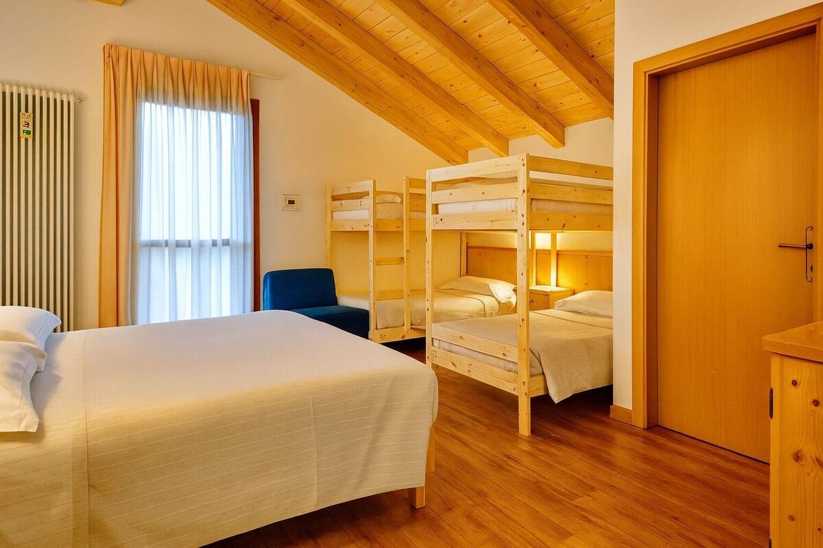 A room with a large bed, three bunk beds, a chair, wooden floors, and a wooden door.