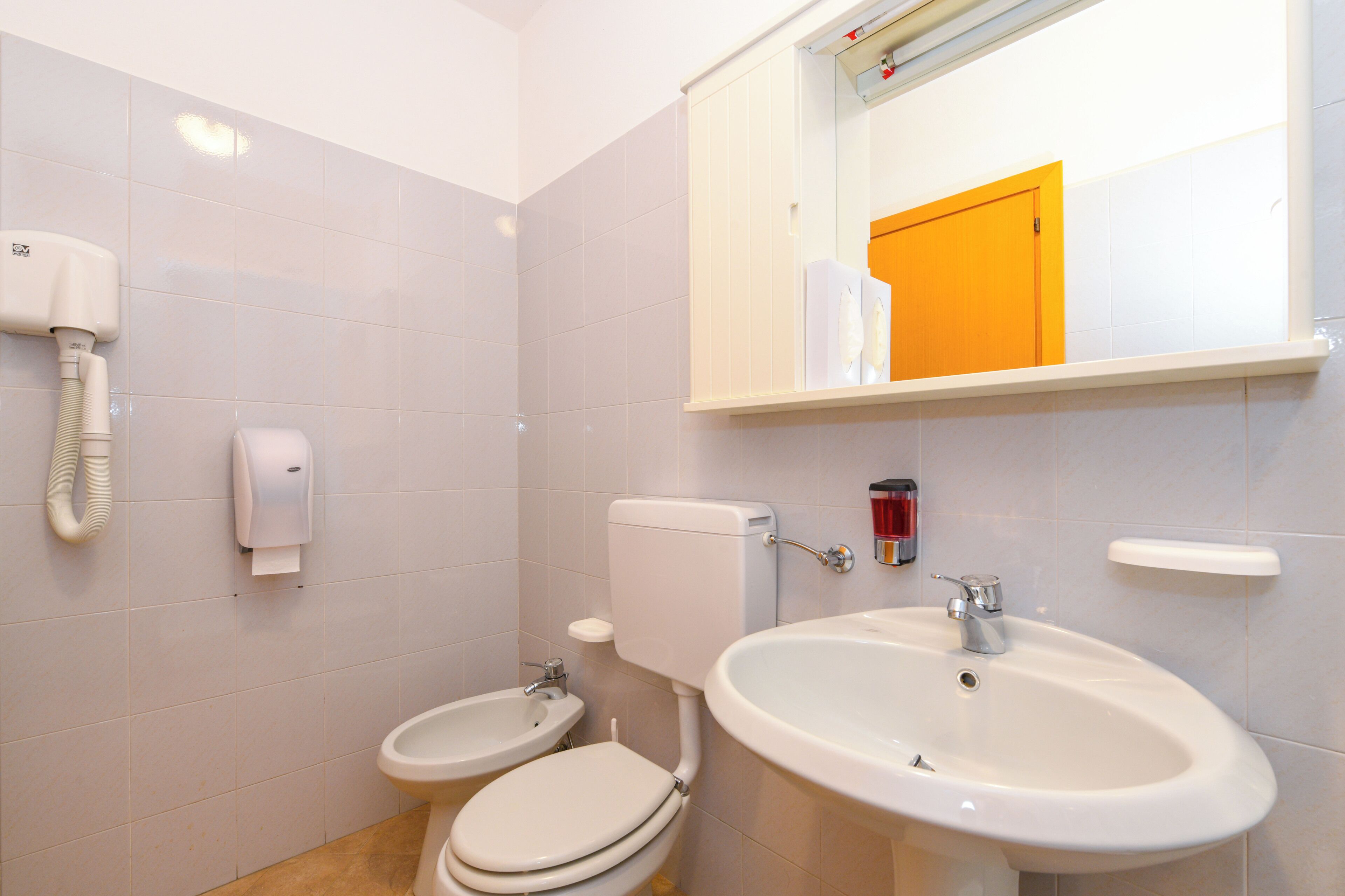 Een badkamer met toilet, bidet, wastafel en een spiegel boven de wastafel.