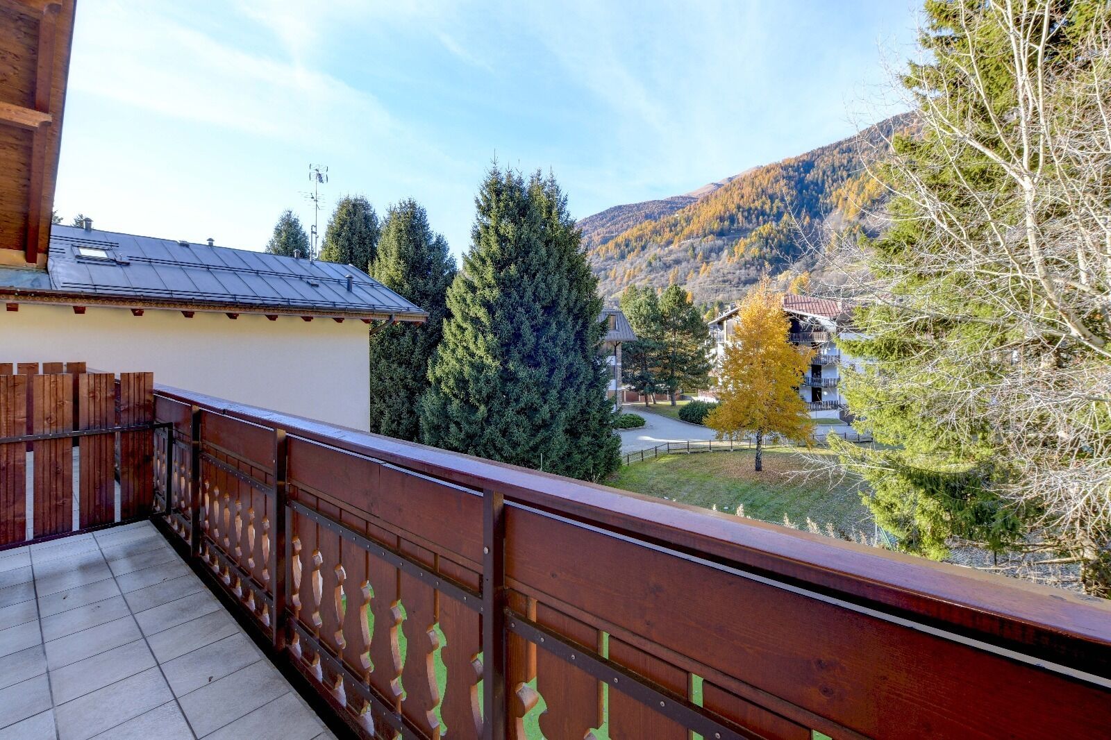 Ein Balkon mit Holzwertung, der auf eine gebirgige Landschaft mit Bäumen und Gebäuden blickt.