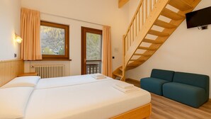 A bedroom with a wooden bed, a blue sofa, a wooden staircase, and a TV mounted on the wall. - Hotel Bleis (Ponte di Legno)
