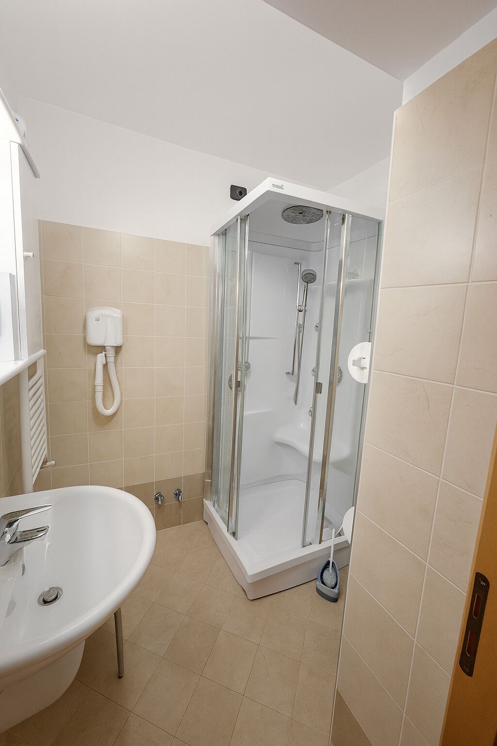 Un baño con cabina de ducha de vidrio, lavamanos blanco y azulejos color beige.