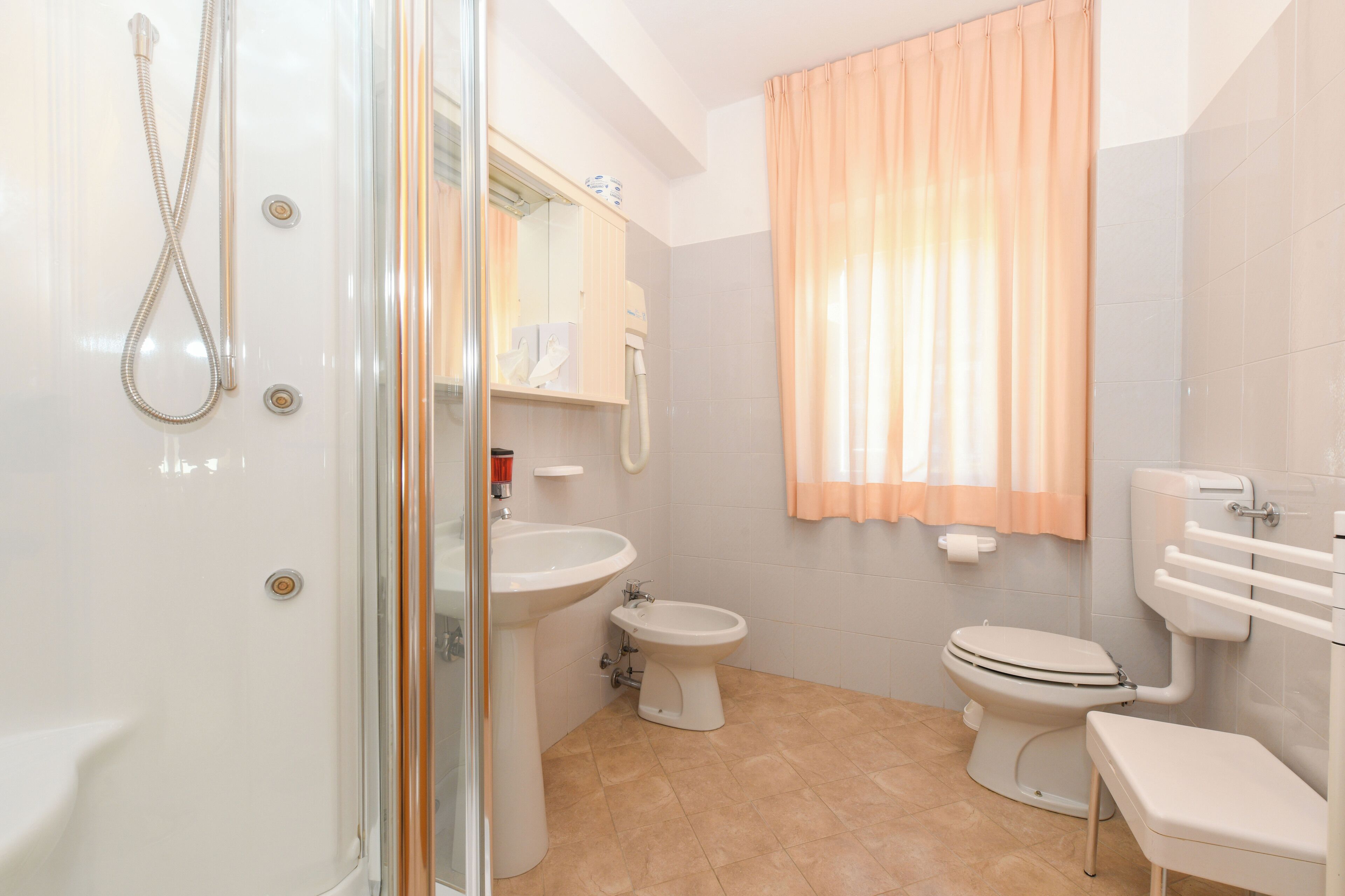 A bathroom with a shower, sink, bidet, toilet, and a glass-enclosed shower stall.