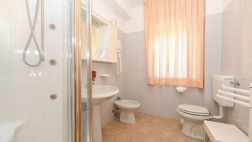 A bathroom with a shower, sink, bidet, toilet, and a glass-enclosed shower stall.