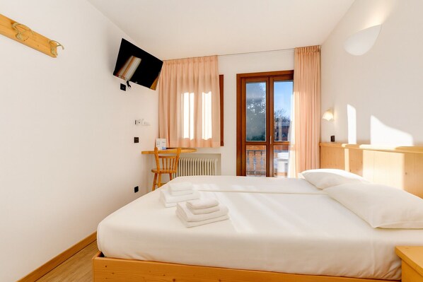 Habitación de hotel con cama, escritorio, silla, televisión y ventana con cortinas.