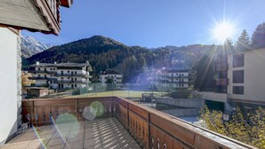 A balcony with a view of a mountainous landscape, a tennis court, and residential buildings. - Hotel Bleis (Ponte di Legno)