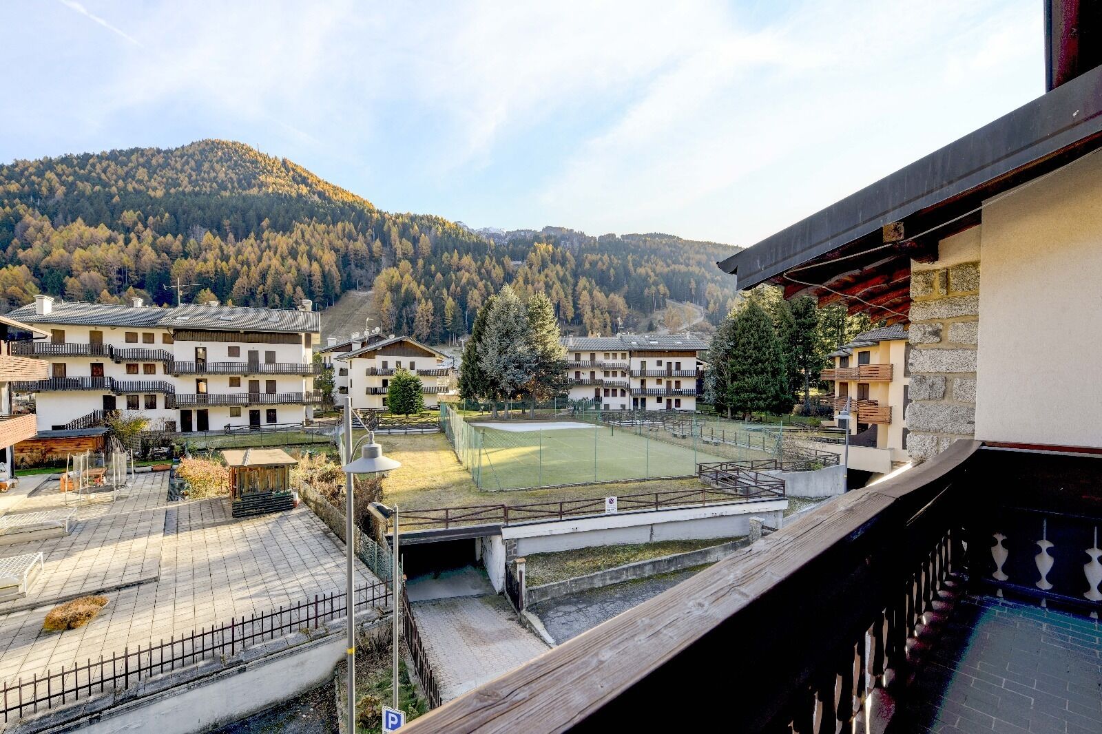A view of a residential area with multiple buildings, a tennis court, and a mountainous backdrop.