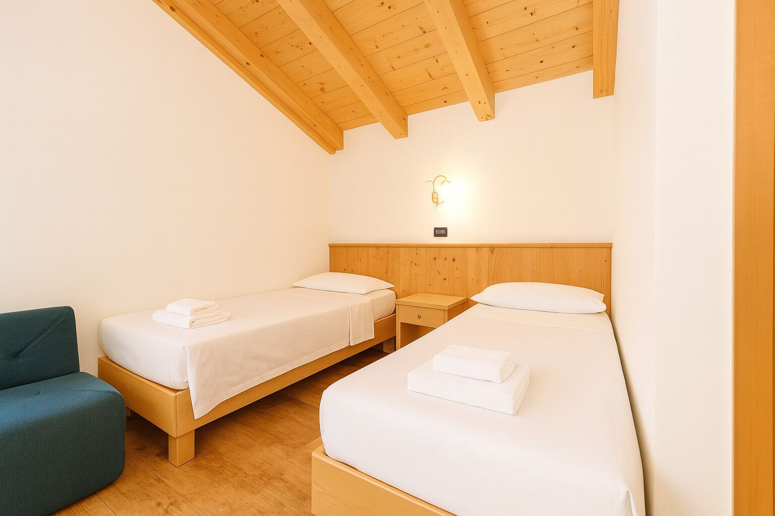 A room with two single beds, wooden headboards, a small bedside table with a lamp, and a blue chair.