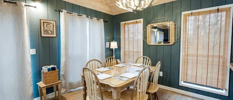 A dining area with a wooden table, chairs, a chandelier, curtains, and a mirror.