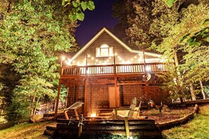 A wooden cabin with a porch, a fire pit, and string lights.