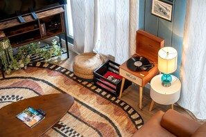A cozy living room with a wooden coffee table, a small side table with a lamp, a record player, and a bookshelf.