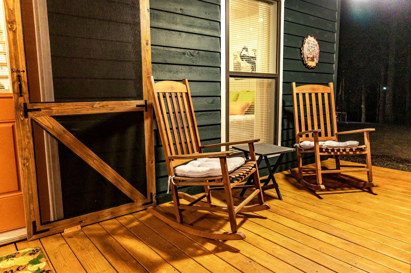A wooden deck with two rocking chairs and a small table, a window with blinds, and a door with a 'Slide' sign.