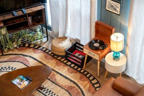 A cozy living room with a wooden coffee table, a small side table with a lamp, a record player, and a bookshelf.