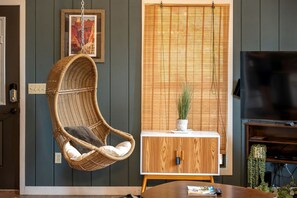 A room with a hanging chair, a television, a cabinet, and a window with blinds.