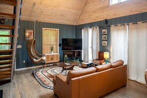 Un salon avec un canapé, un fauteuil suspendu, un téléviseur et un plafond en bois.