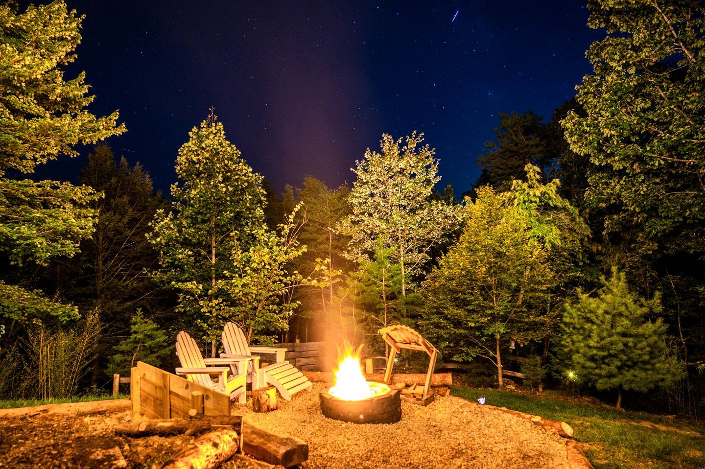 A campfire with chairs and a fire pit in a forest at night.