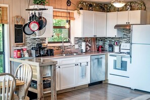 A modern kitchen with white cabinets, a stainless steel dishwasher, a built-in oven, and a hanging pot rack.