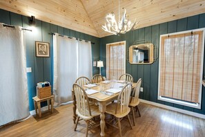 A dining area with a wooden table, chairs, a chandelier, curtains, and a mirror.