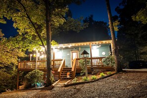 Une cabane en bois avec un porche, entourée d’arbres, de nuit.