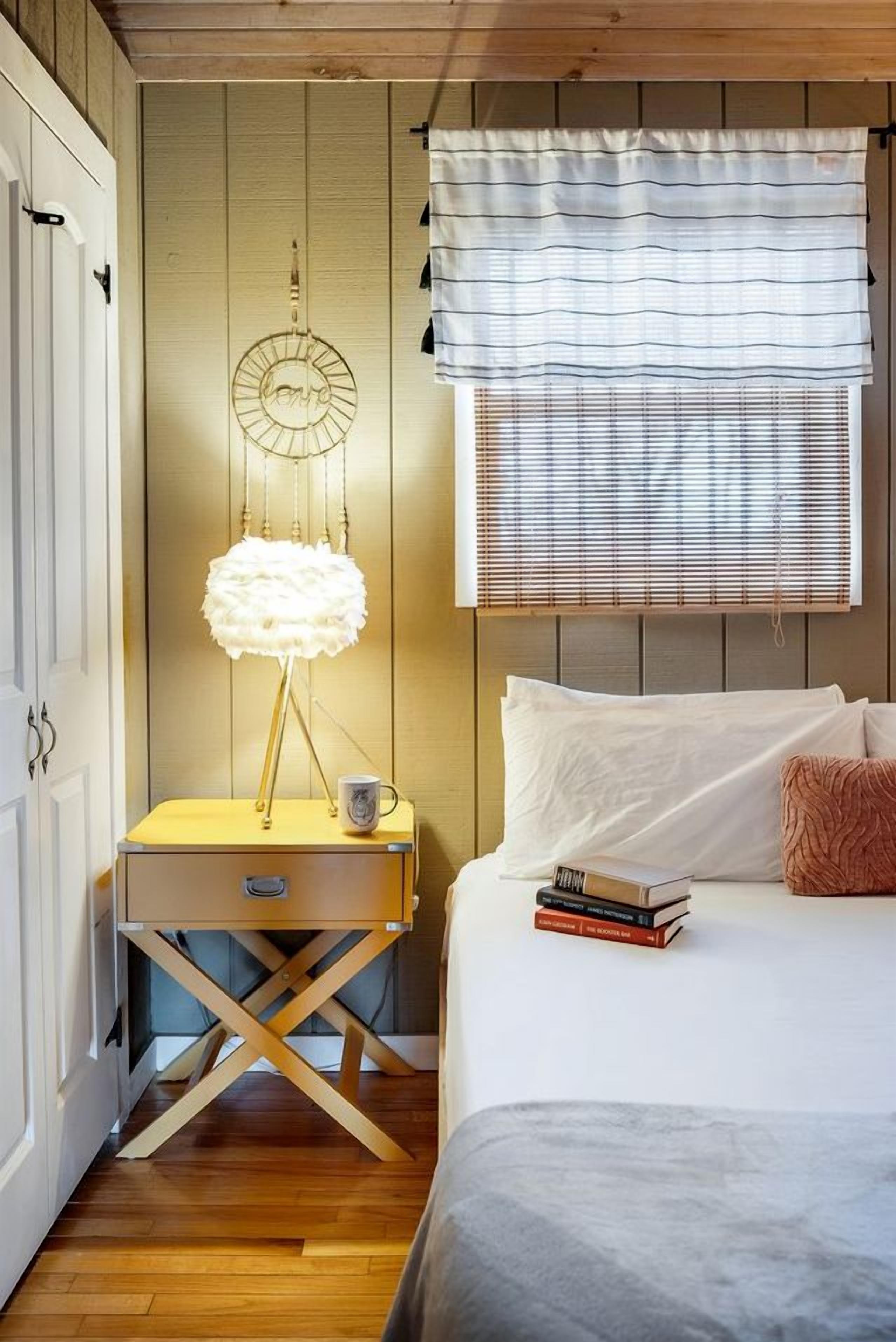Et soveværelse med seng, sengebord, lampe og vindue med persienner.