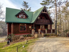 A cabin with a green roof, stone foundation, and a wooden deck.