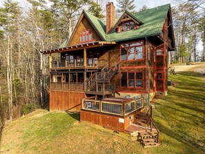 A wooden cabin with a balcony, a covered porch, and a chimney.