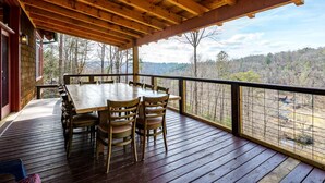 A wooden deck with a table and chairs, overlooking a forested landscape.
