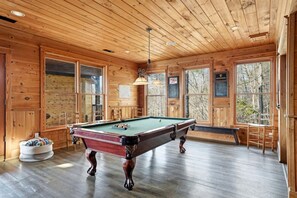 A wooden interior with a pool table, wooden walls, and large windows. - Luxury Three-Story Riverfront Cabin Rental for Groups in Blue Ridge Region of Georgia (Blue Ridge)