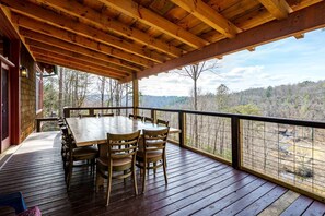 A wooden deck with a table and chairs, overlooking a forested landscape.