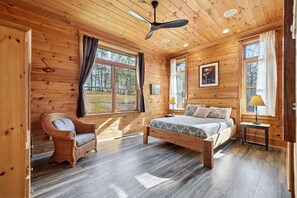 A wooden cabin bedroom with a bed, a wicker chair, and a ceiling fan.