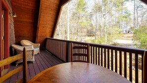 A wooden deck with a table and chairs, overlooking a forested area.