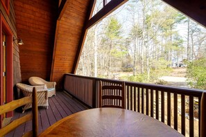 A wooden deck with a table and chairs, overlooking a forested area.