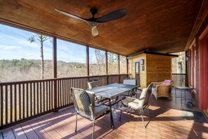 A covered outdoor deck with a table and chairs, a ceiling fan, and a view of the surrounding landscape.