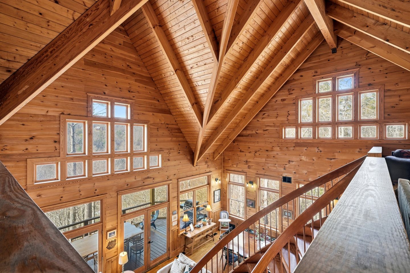 A spacious cabin with a high ceiling, multiple windows, and a wooden staircase.
