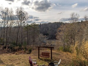 A wooden bench and chairs in a natural setting with trees and a view of a forested area.