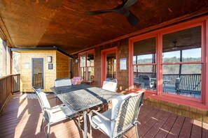 A covered outdoor deck with a table and chairs, a ceiling fan, and large windows.